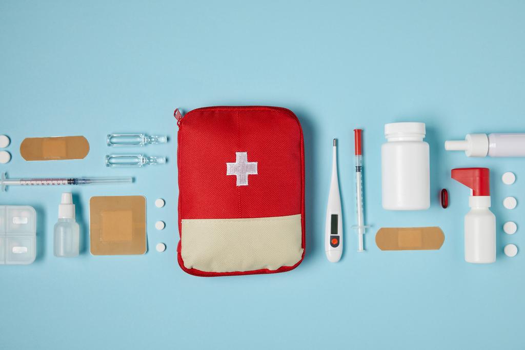 bovenaanzicht van rode EHBO kit bag van blauwe ondergrond met medische benodigdheden - Foto, afbeelding