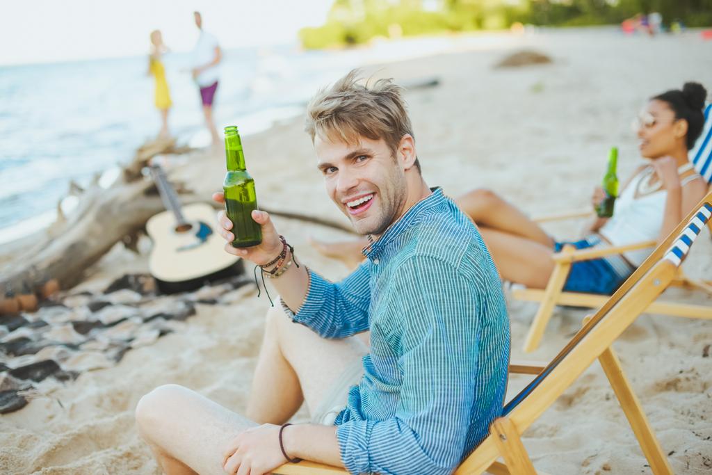 selective focus of group of friends with beer resting on sandy beach together - Photo, Image