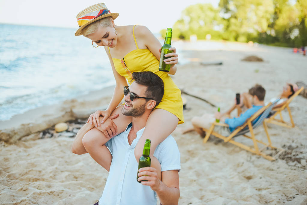 селективное внимание счастливой женщины, сидящей на плечах своих парней и друзей, отдыхающих на пляже
 - Фото, изображение