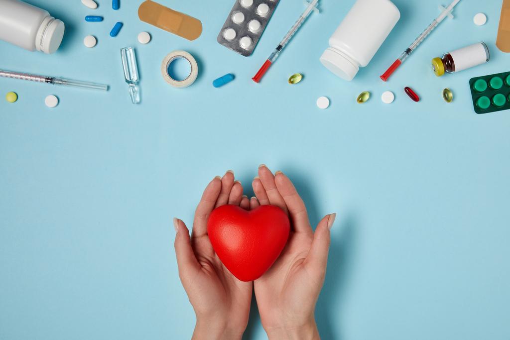 cropped shot of woman holding heart over medicines on blue surface - Photo, Image