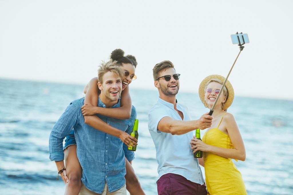 portrait of interracial young friends with beer taking selfie by sea - Photo, Image