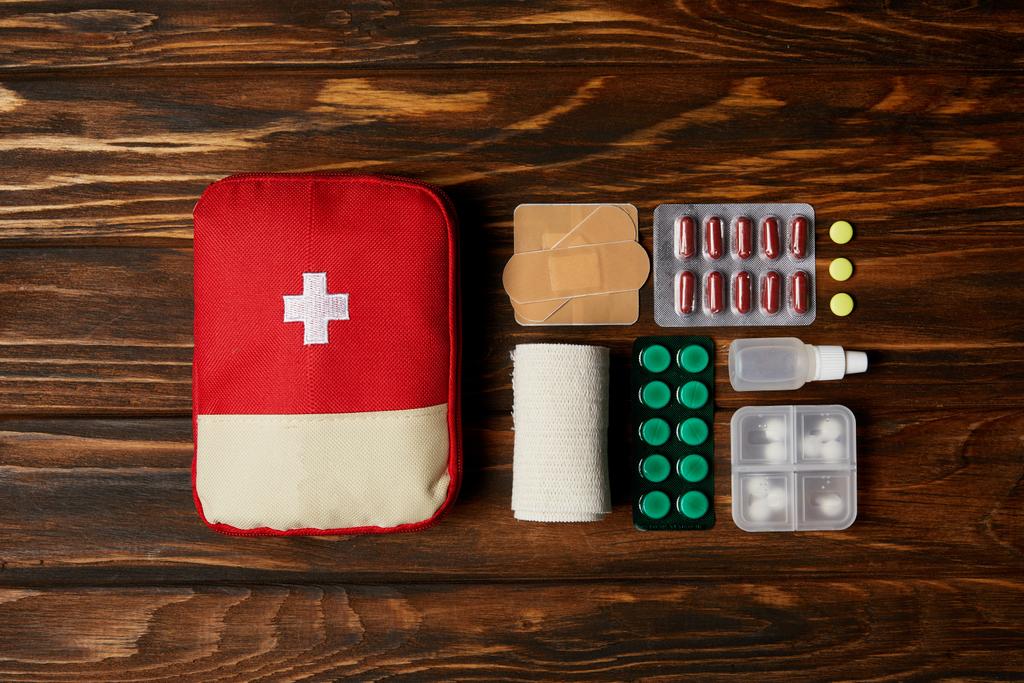 top view of first aid kit composed with various pills and bandage on wooden tabletop - Photo, Image