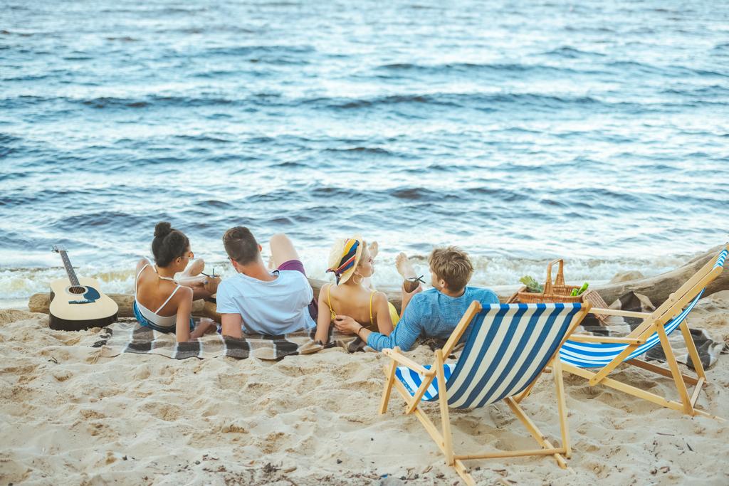 вид на многонациональных друзей, отдыхающих на одеяле на песчаном пляже
 - Фото, изображение