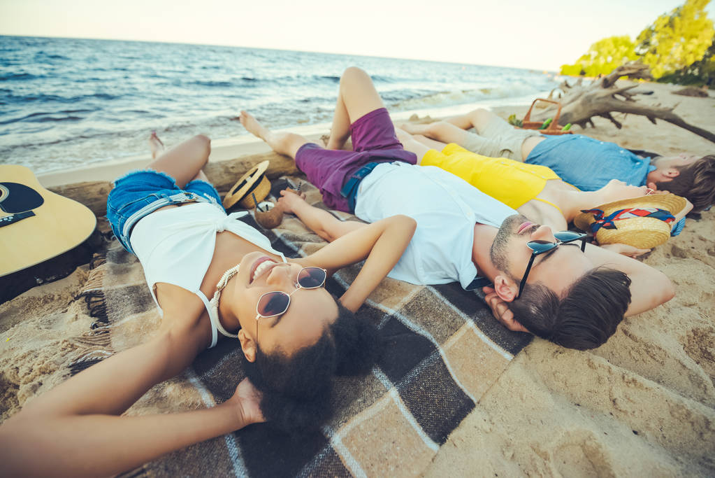 Selektywny fokus wielorasowe młodych ludzi leży na kocu a spędzanie czasu na piaszczystej plaży - Zdjęcie, obraz