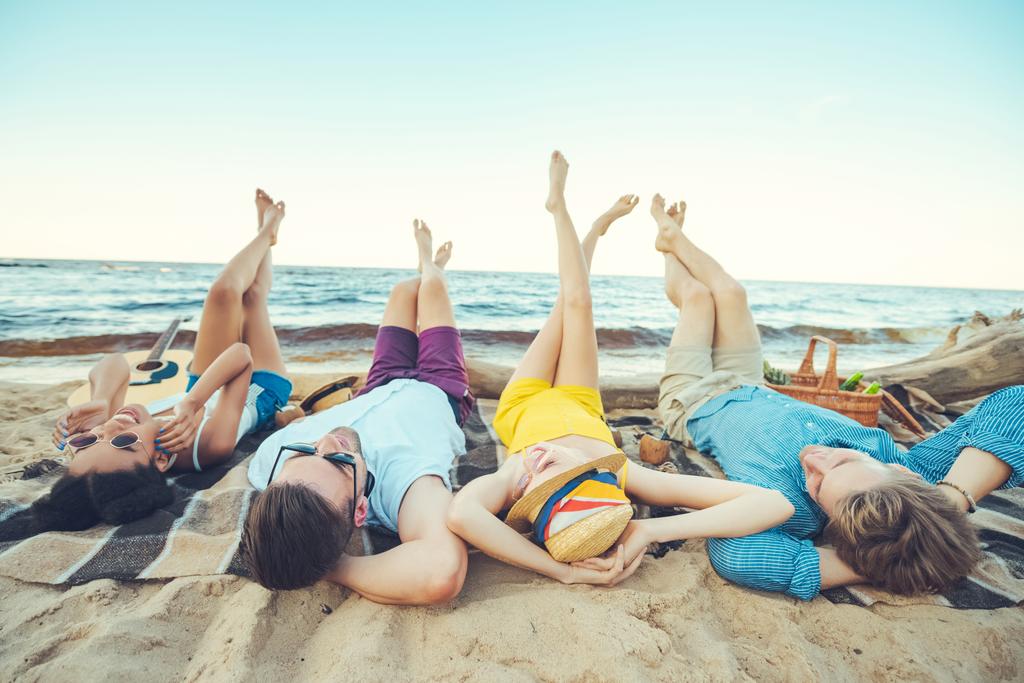 многорасовая молодежь лежит на одеяле, проводя время на песчаном пляже
 - Фото, изображение
