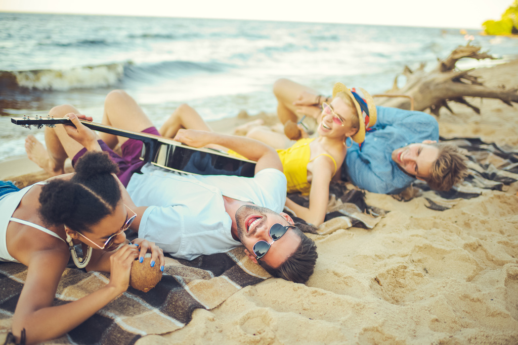 мультикультурні друзі з кокосовими коктейлями та акустичною гітарою відпочивають на піщаному пляжі
 - Фото, зображення