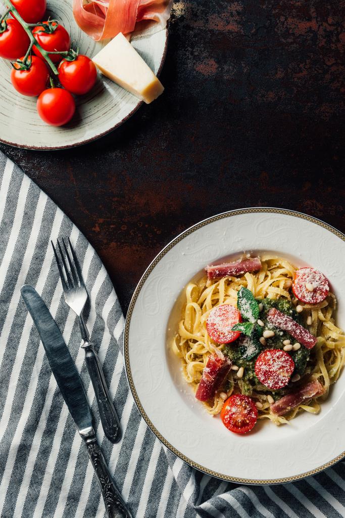 näkymä ylhäältä levyt pastaa ja jamon, parmesan ja jamon pöydällä keittiöpyyhkeellä, haarukka ja veitsi
 - Valokuva, kuva