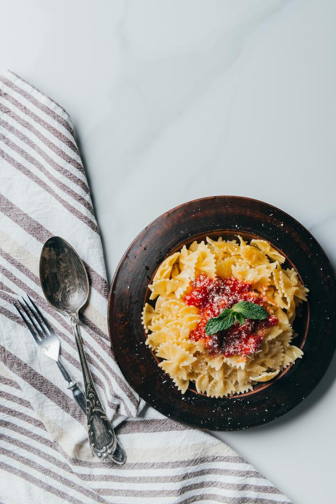 vue de dessus des pâtes aux feuilles de menthe et sauce recouverte de parmesan râpé sur table en marbre avec fourchette, couteau et torchon
  - Photo, image