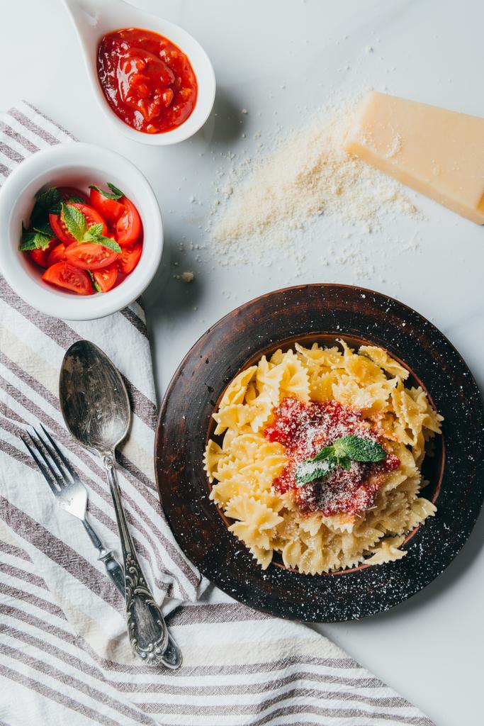 vista dall'alto del piatto con pasta, parmigiano grattugiato, ciotole con salsa e pomodorini sul tavolo di marmo
  - Foto, immagini