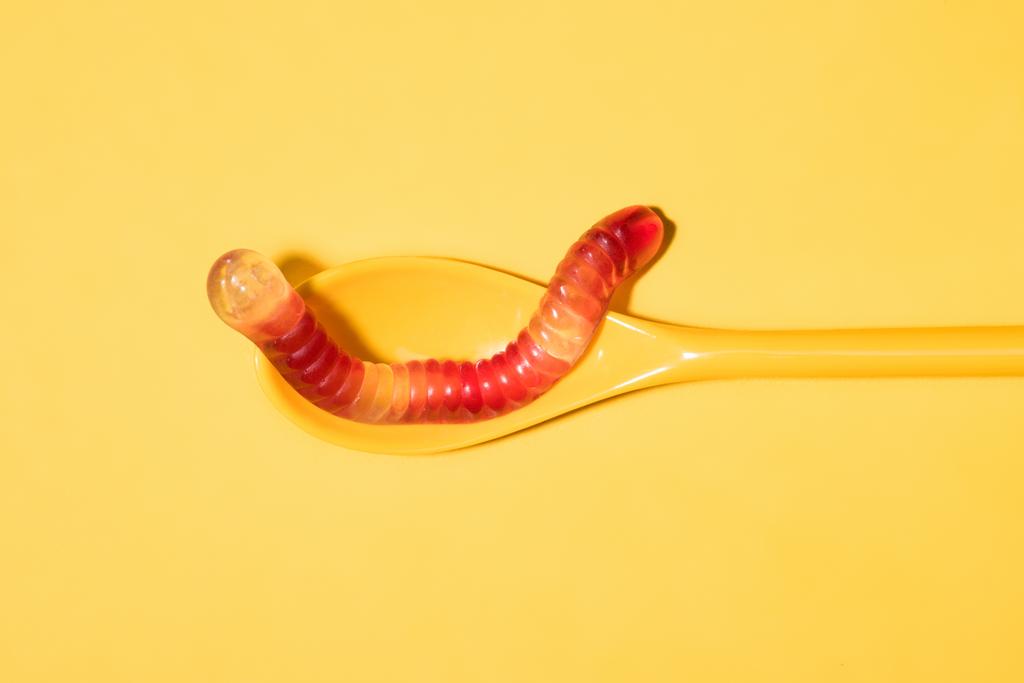 bovenaanzicht van gummy worm op lepel en op geel - Foto, afbeelding