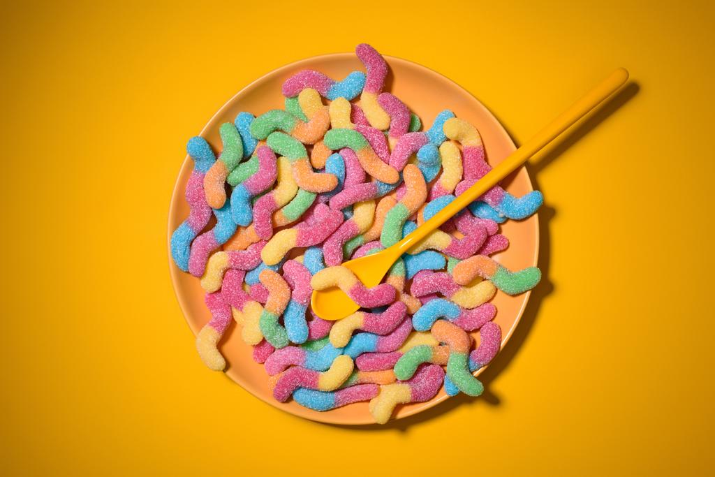 top view of gummy worms with spoon on plate and on yellow - Photo, Image