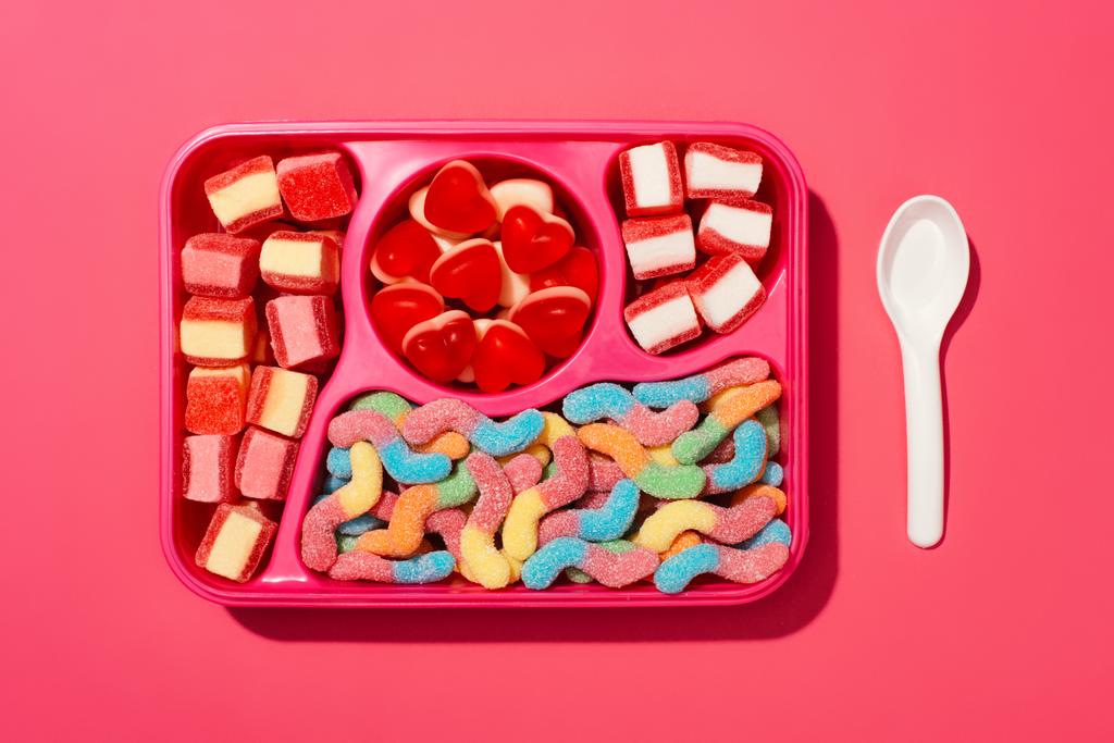 vista superior de doces de goma na bandeja de plástico na superfície rosa
 - Foto, Imagem