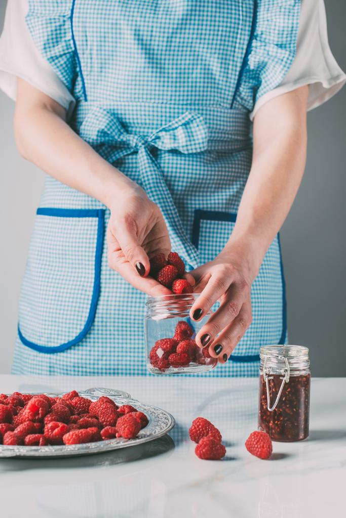 imagen recortada de la mujer en delantal haciendo mermelada de frambuesas sobre la mesa
  - Foto, Imagen