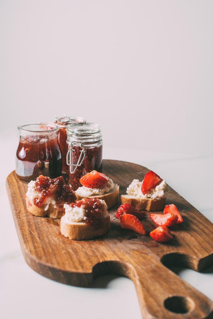zblízka pohled na prkénku s ovocným džemem ve sklenicích a sendviče s tvarohovým krémem a jam na grey - Fotografie, Obrázek