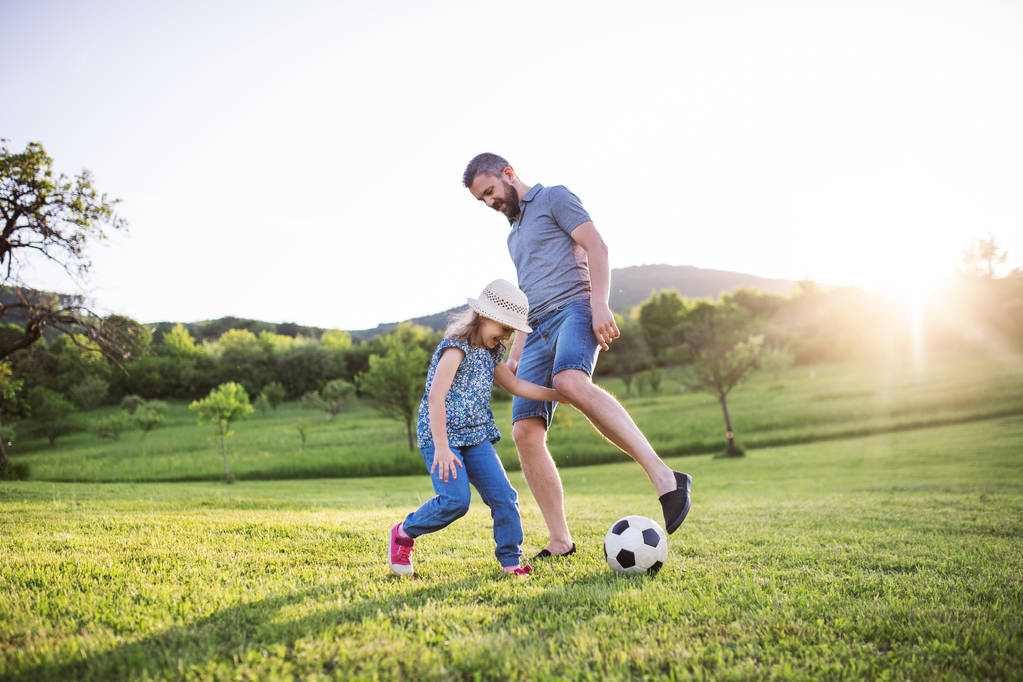 Ο πατέρας με μια μικρή κόρη παίζει με μια μπάλα στην ανοιξιάτικη φύση. - Φωτογραφία, εικόνα