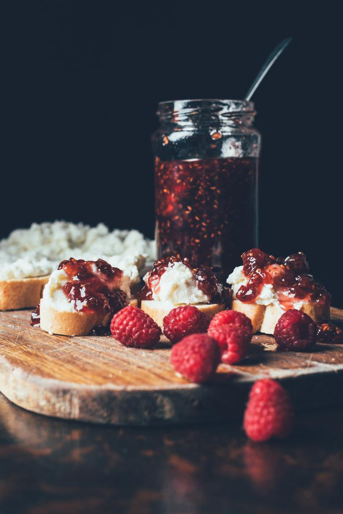 selective focus of raspberries, sandwiches with fruit jam and cream cheese on cutting on black  - Photo, Image