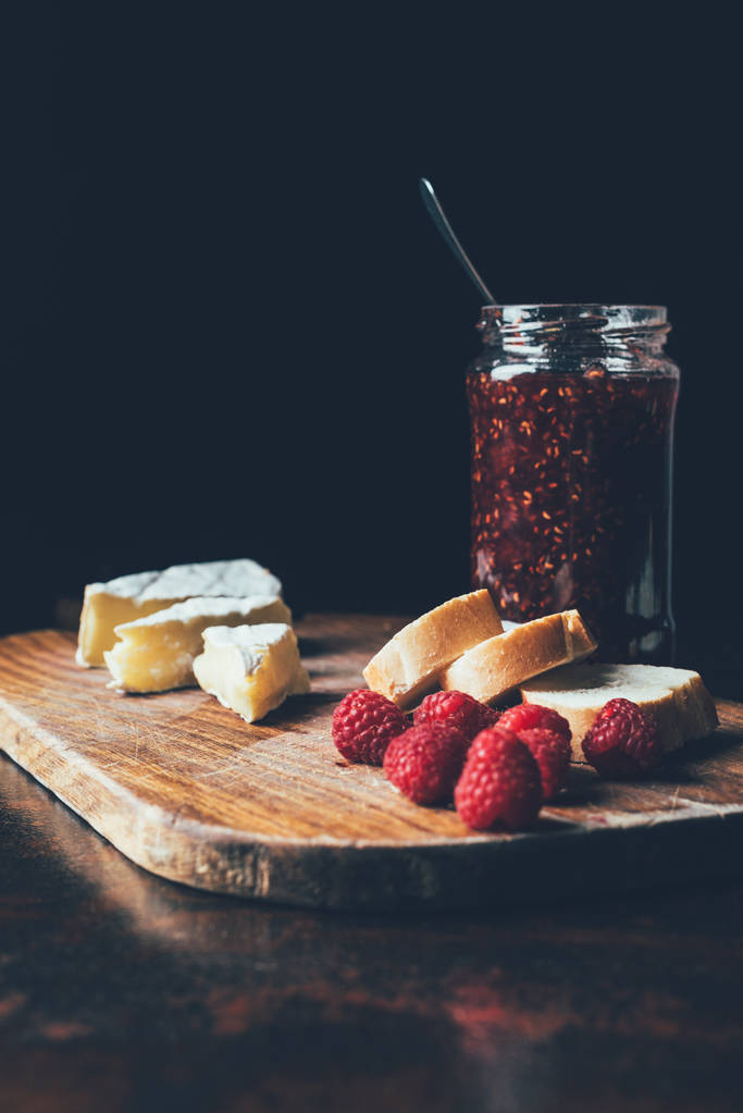 close up view of brie, raspberries, jam in jar and baguette on cutting board at table  - Photo, Image