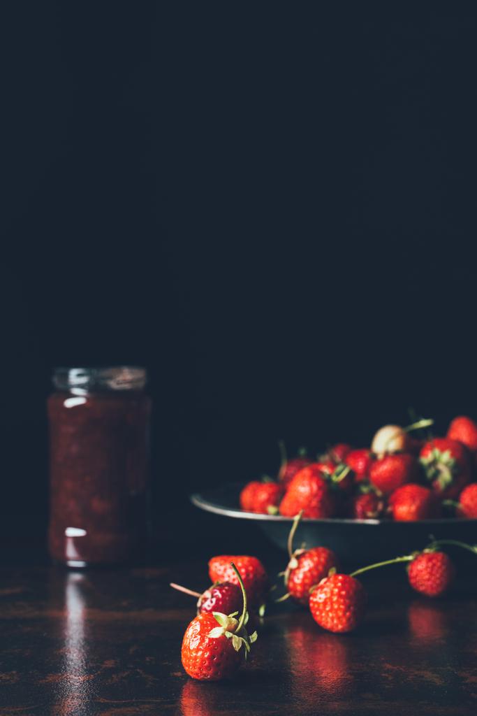 selektiver Fokus von Erdbeeren im Silbertablett und Fruchtmarmelade im Glas auf Schwarz  - Foto, Bild