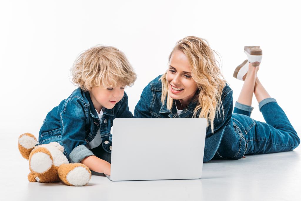 moeder en zoon met behulp van laptop op verdieping op wit - Foto, afbeelding
