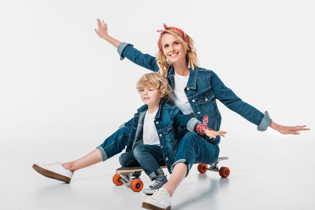 Gelukkig moeder en zoon zittend op een skateboard en doen alsof ze vliegen op wit - Foto, afbeelding