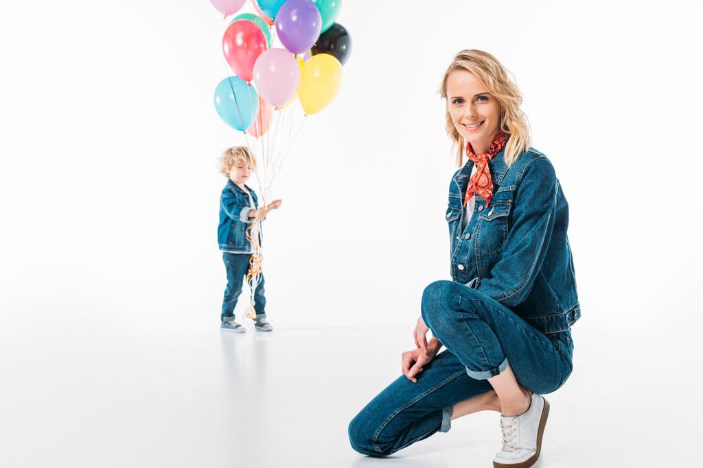son walking with balloons and mother squatting on foreground on white - Photo, Image