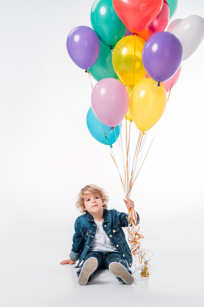 adorable boy sitting and holding bundle of balloons on white - Photo, Image