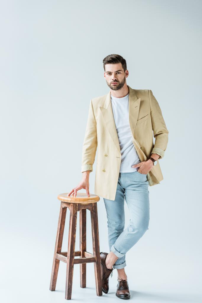 Uomo alla moda fiducioso appoggiato su sgabello su sfondo bianco
 - Foto, immagini