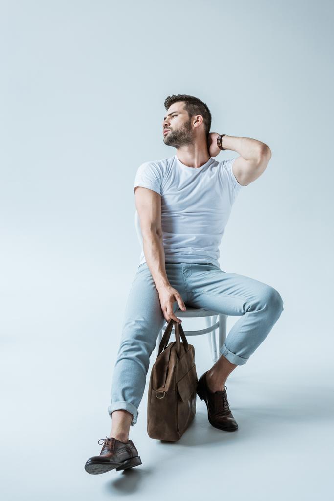 Красивий бородатий чоловік сидить на стільці і тримає портфель на білому тлі
 - Фото, зображення