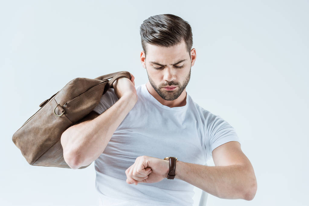 Hombre confiado de moda sosteniendo el maletín y comprobando su reloj aislado sobre fondo blanco
 - Foto, imagen