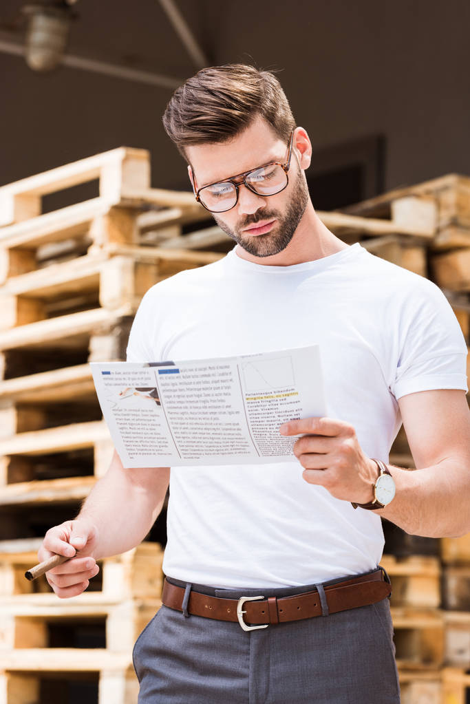 Hombre de negocios barbudo guapo sosteniendo cigarro y leyendo informe por paletas de madera
 - Foto, imagen
