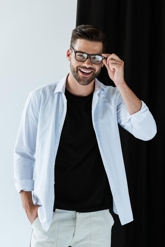 Stilvoller junger Mann lächelt und trägt Brille am schwarzen Vorhang - Foto, Bild