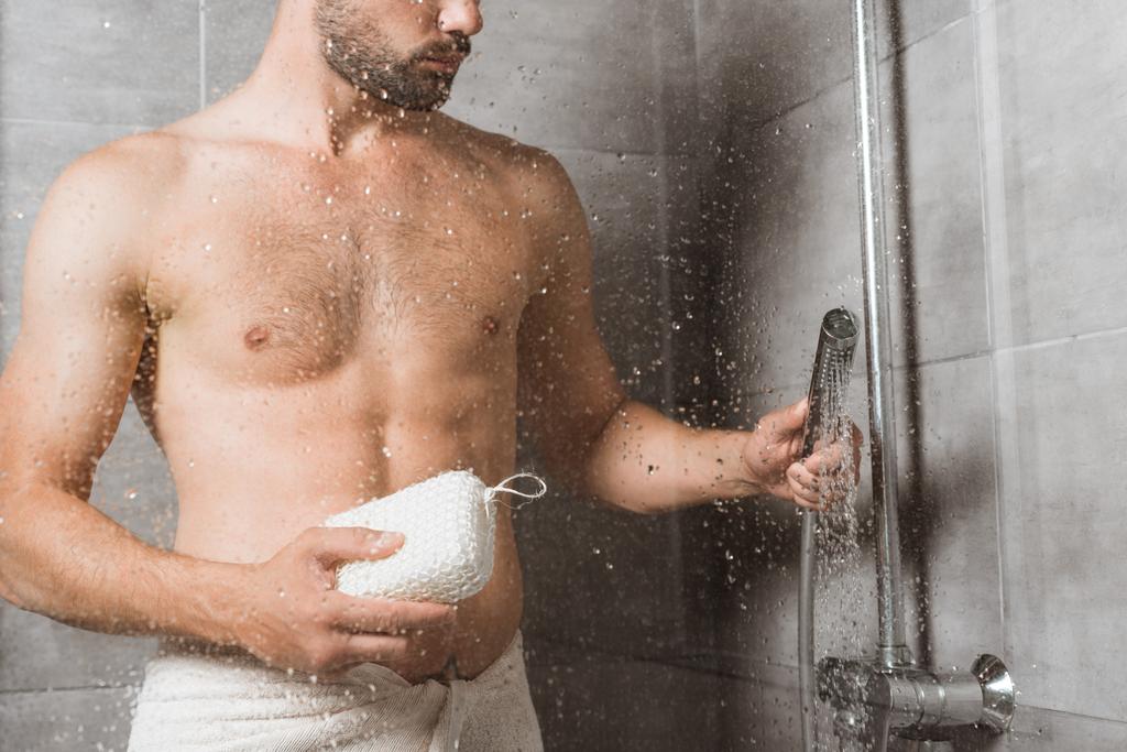Handsome bearded man holding sponge behind shower glass - Foto, afbeelding