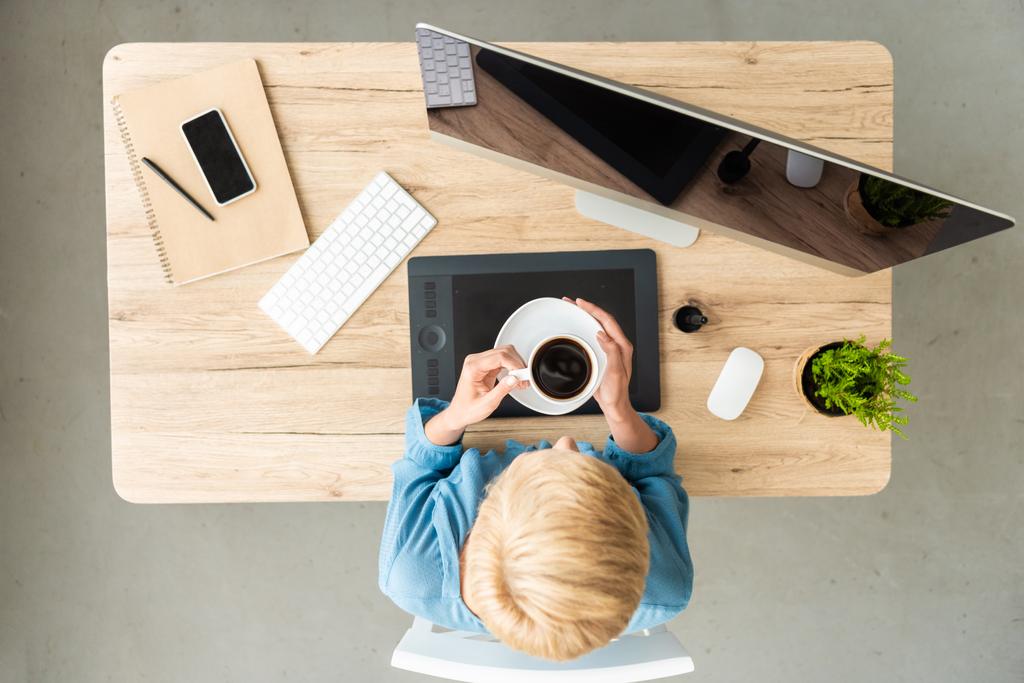 felülnézete női szabadúszó gazdaság csésze kávé asztal, grafikus tabletta, a smartphone és a számítógép otthoni iroda  - Fotó, kép