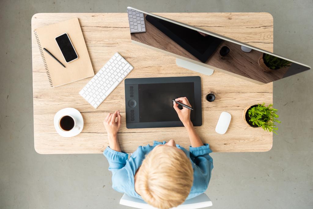 bovenaanzicht van vrouwelijke freelancer bezig met grafisch tablet aan tafel met een kopje koffie, een smartphone en een computer thuis bureau  - Foto, afbeelding