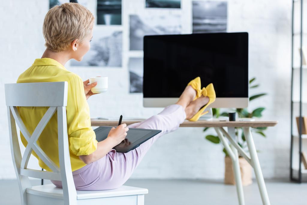 foyer sélectif de la femme pigiste boire du café et en utilisant une tablette graphique à la table avec ordinateur au bureau à domicile
  - Photo, image
