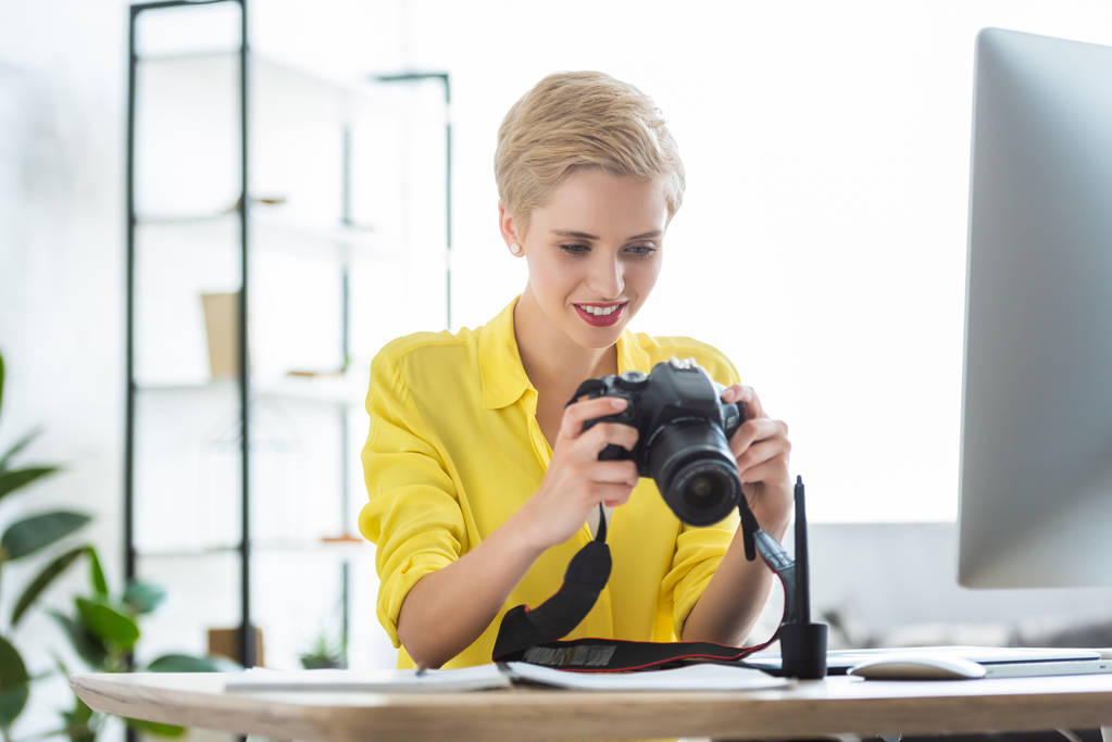 lachende vrouwelijke fotograaf op zoek naar camera scherm aan tafel met computer  - Foto, afbeelding