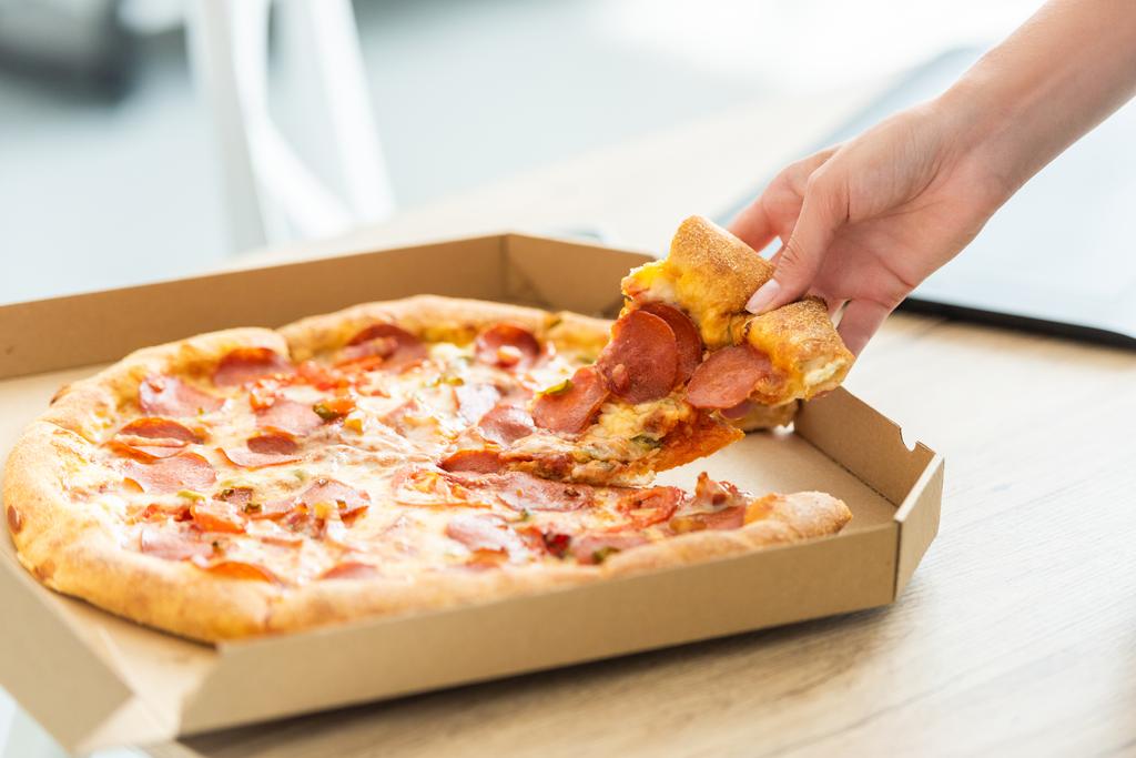 abgeschnittenes Bild einer Frau, die Pizzascheiben aus Schachtel am Tisch nimmt  - Foto, Bild