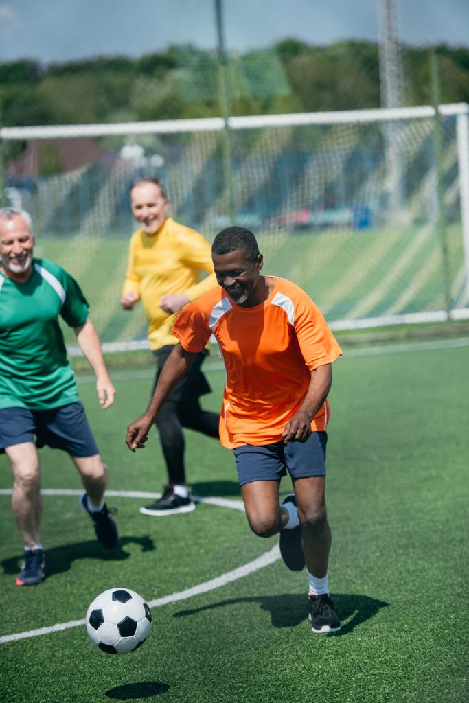 mnohonárodnostní starci hrát fotbal společně na zelené louce - Fotografie, Obrázek
