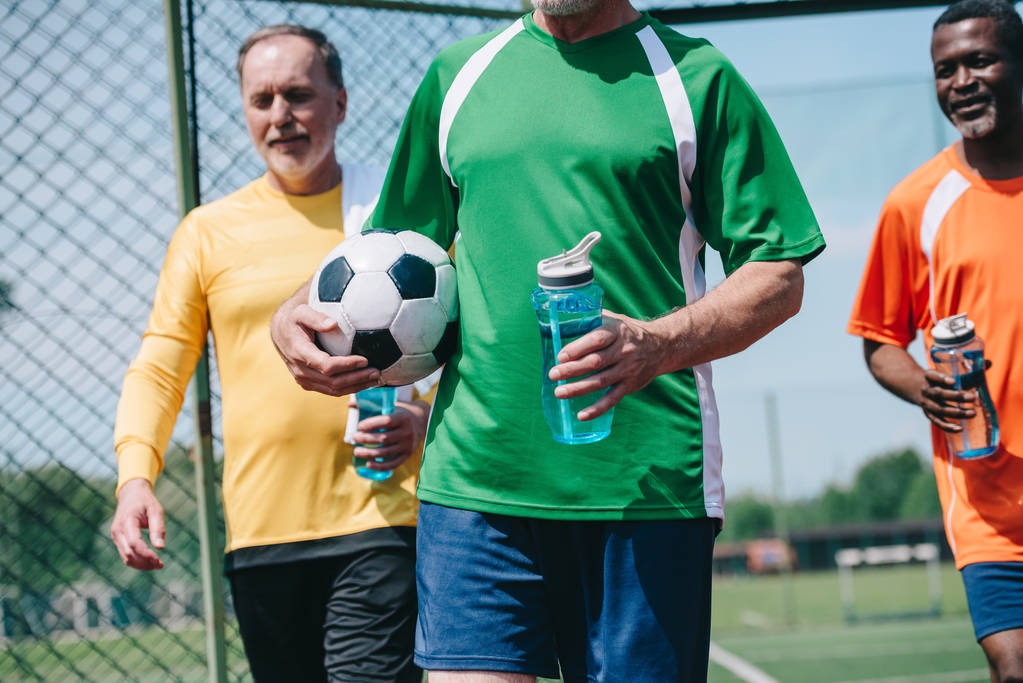 vista parziale di uomini anziani multiculturali con bottiglie d'acqua sportive e pallone da calcio
 - Foto, immagini