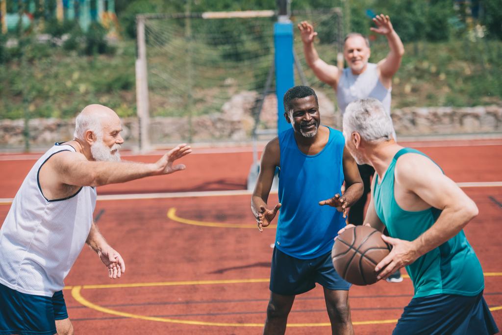 Sex tussen verschillendre rassen oudere sporters spelen basketbal samen op speelplaats - Foto, afbeelding