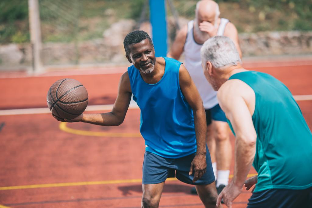πολυφυλετικές ηλικιωμένους άνδρες παίζουν μπάσκετ μαζί σε παιδική χαρά θερινή ημέρα - Φωτογραφία, εικόνα