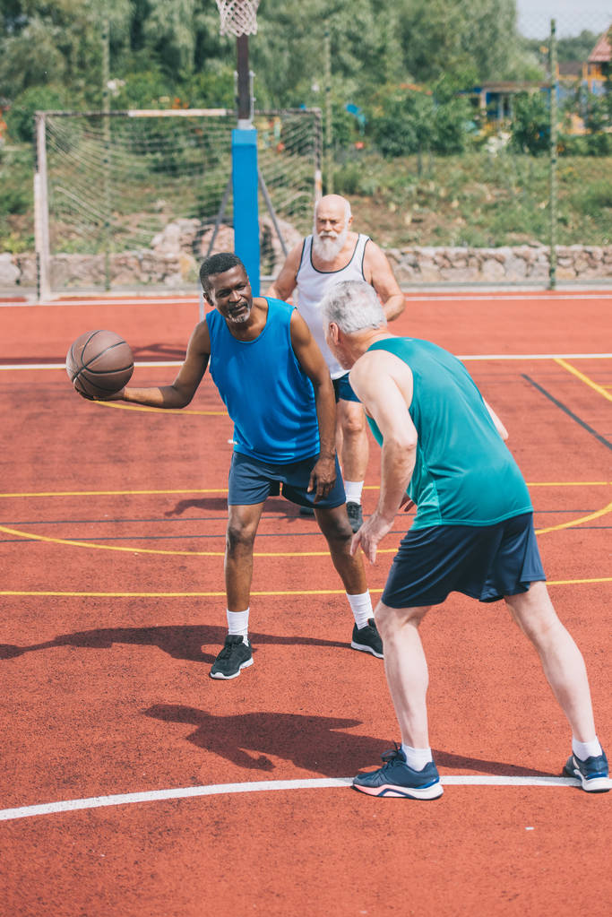 monirotuinen vanhukset miehet pelaavat koripalloa yhdessä leikkikentällä kesäpäivänä
 - Valokuva, kuva