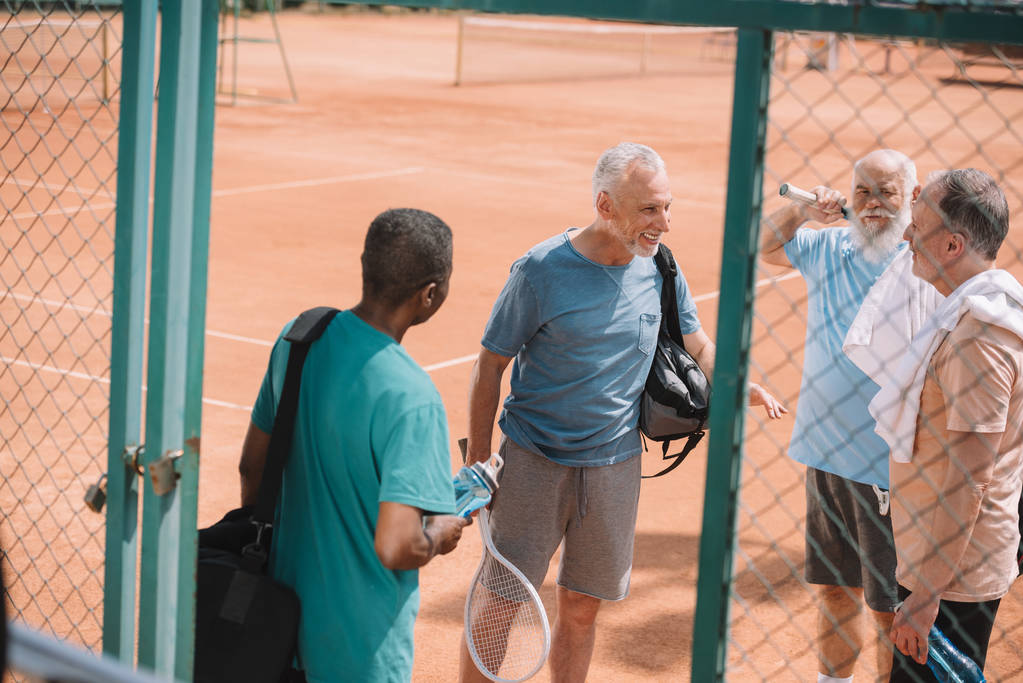 многорасовая группа пожилых друзей с теннисным оборудованием на корте
 - Фото, изображение