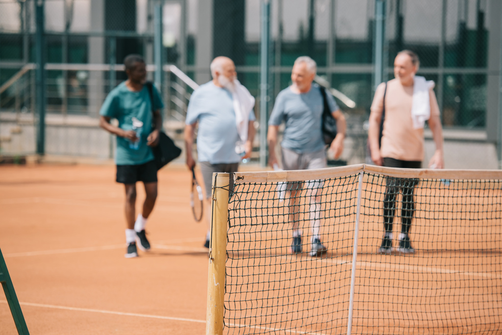 επιλεκτική εστίαση της πολυφυλετικής ηλικιωμένοι φίλοι με τον εξοπλισμό τένις στο γήπεδο - Φωτογραφία, εικόνα