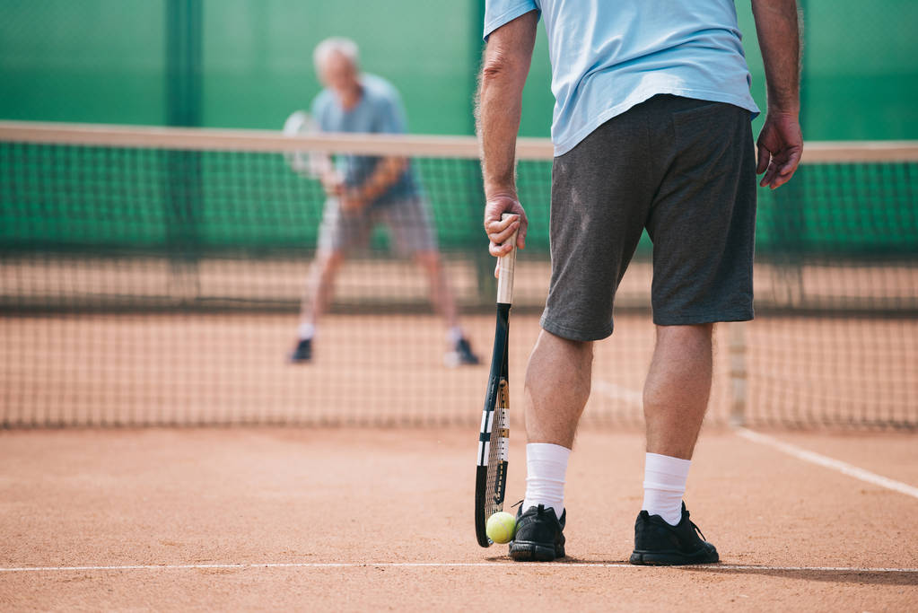 частичный вид старика, играющего в теннис с другом в суде
 - Фото, изображение