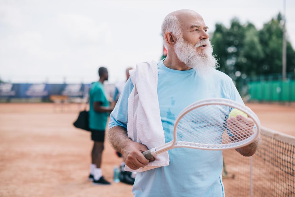 selective focus of bearded old man with towel and tennis racquet on court - Photo, Image
