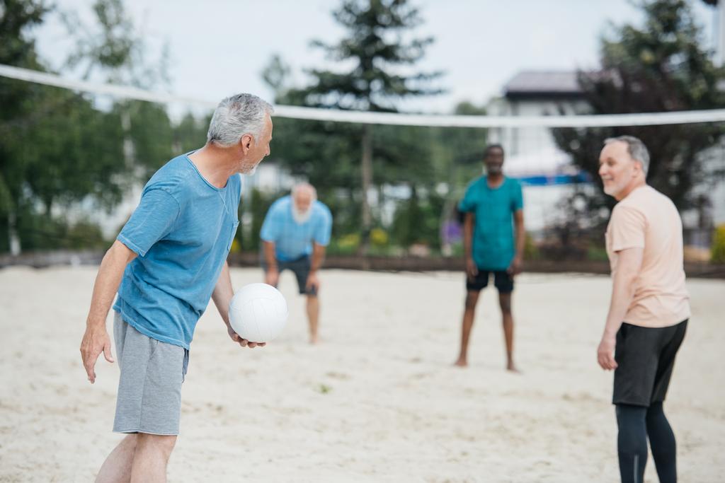 focus selettivo di vecchi amici multiculturali che giocano a pallavolo sulla spiaggia nella giornata estiva
 - Foto, immagini