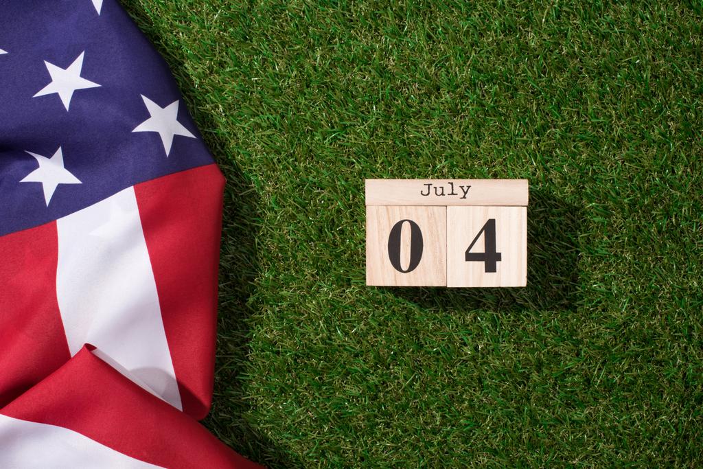 Draufsicht auf amerikanische Flagge und hölzernen Kalender mit Datum des 4. Juli auf grünem Rasen, Amerikas Konzept zum Unabhängigkeitstag - Foto, Bild