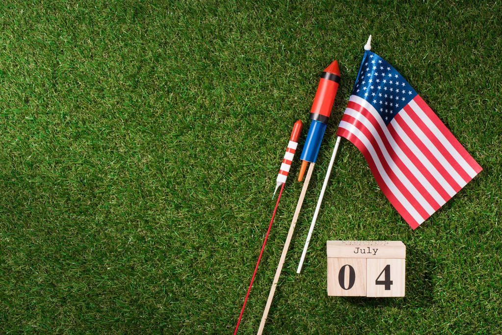 επίπεδη lay με αμερικανική κοντάρι σημαίας, ξύλινο ημερολόγιο με 4η Ιουλίου ημερομηνίας και πυροτεχνήματα για την πράσινη χλόη, Αμερική έννοια ημέρα ανεξαρτησίας - Φωτογραφία, εικόνα