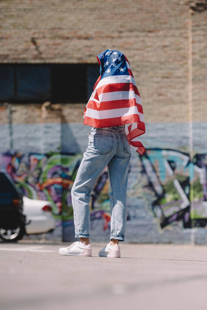 Rückansicht einer Frau mit amerikanischer Flagge in den Händen, die auf der Straße steht, Ferienkonzept 4. Juli - Foto, Bild